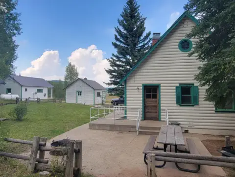 Exterior view of several log cabins and a picnic table on a grassy area under a partly cloudy sky.