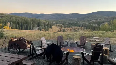 A fire pit surrounded by chairs with a mountain landscape in the background.