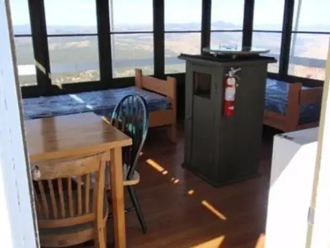 The interior of a fire lookout tower showing beds, a table, and a fire finder.