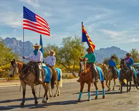 A group of horse riders carrying flags in a parade with mountains in the background.