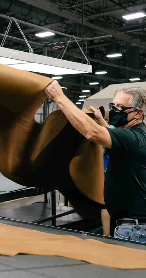 A man wearing a face mask examines a large hide in a workshop.