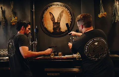 Two bartenders work behind a bar under a rabbit portrait.