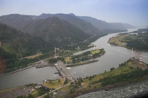 An aerial view of a large dam on a winding river surrounded by mountains.
