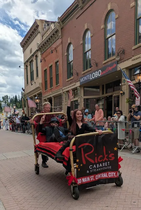 People riding in a decorated bed on wheels during a street event.