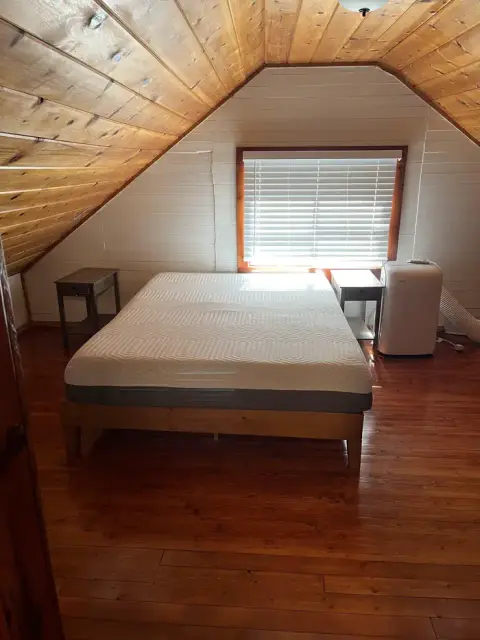 A bedroom with a slanted wooden ceiling and a bed in the center.