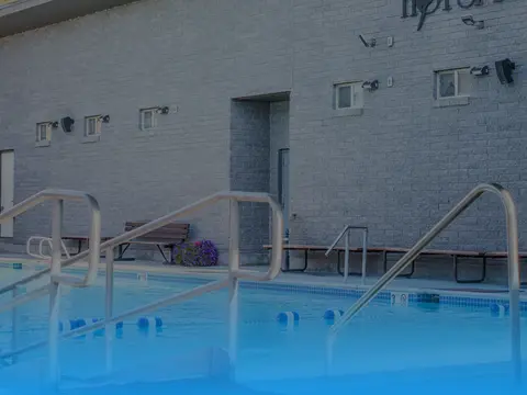 An outdoor swimming pool with metal handrails and a brick building in the background.