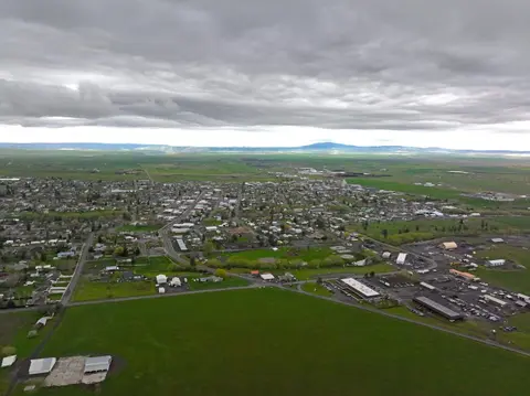 An aerial view of a town surrounded by green fields under a cloudy sky.