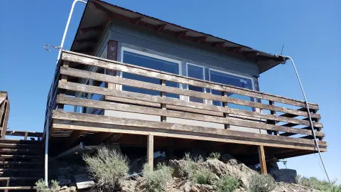 Exterior view of a wooden lookout tower with large windows and a wrap-around balcony against a clear blue sky.
