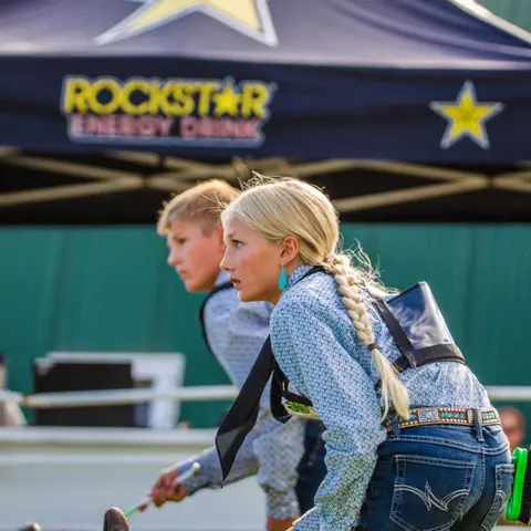 A young girl with a braid is leaning forward outdoors with a boy behind her.