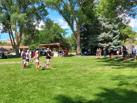 People playing cornhole on a grassy lawn with trees in the background.