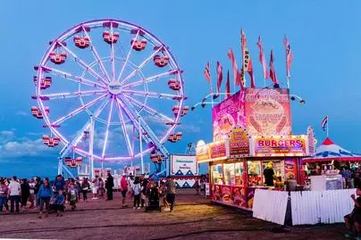 A brightly lit ferris wheel and carnival food stand at an evening fair.