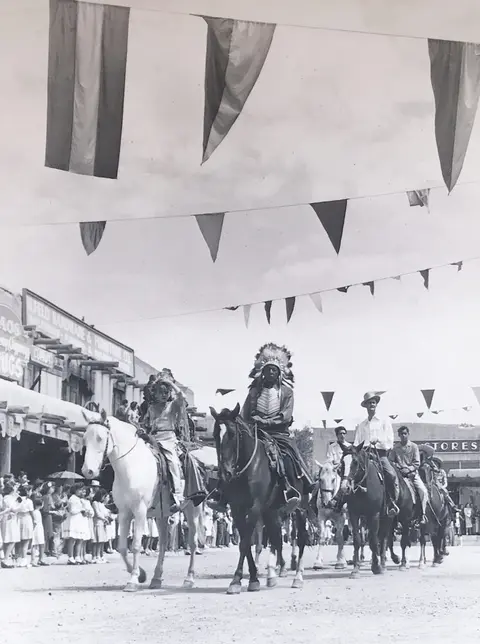Historic photo of people on horseback in a parade with flags overhead.