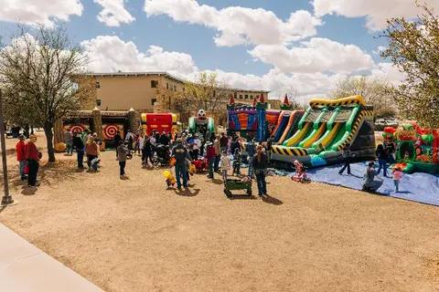 People gather at an outdoor festival featuring inflatable bounce houses and slides.