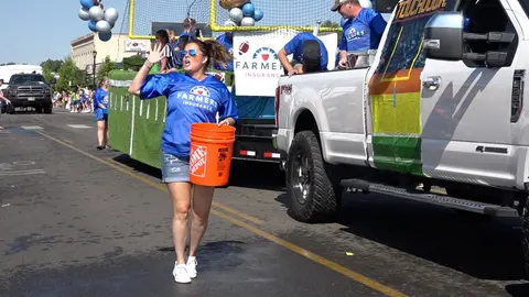 A woman carrying a bucket walks along a parade float.