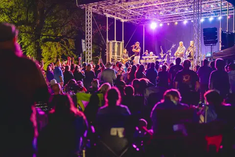A crowd watches a band perform on an outdoor stage at night.