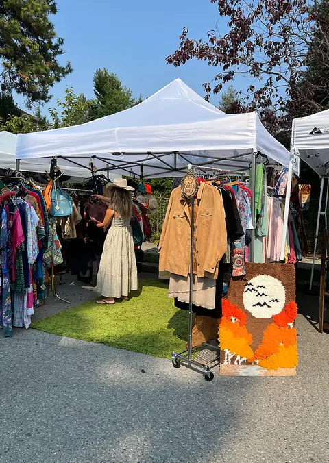 A person browses clothing at an outdoor market booth.