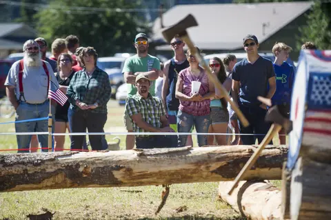 A crowd watches an axe throwing event outdoors.