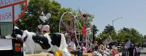 A parade float features large animal models, including a cow, pig, and rooster.