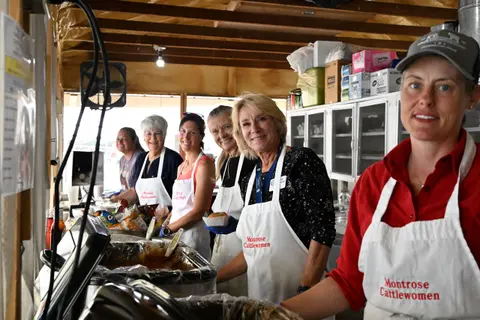 Several women wearing aprons work inside a food booth.