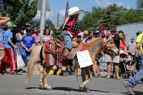 A child in a cowboy hat rides a decorated pony in a parade.