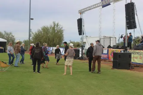 People dance on the grass in front of an outdoor stage with sound equipment.