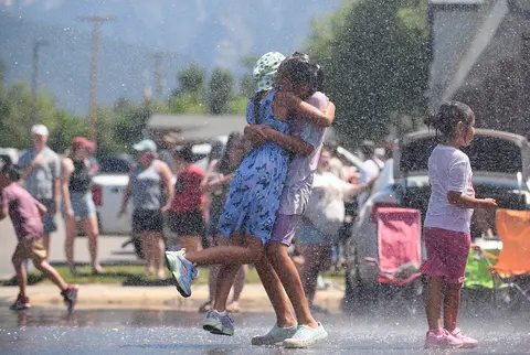 Children play and embrace in the spray of water outdoors.