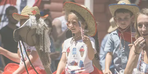 Children wearing cowboy hats and holding flags on a float during an event.