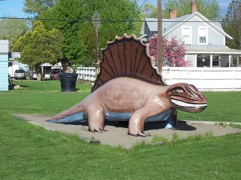 A large Dimetrodon statue sits on a gravel patch in a grassy yard.