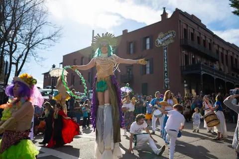 A person on stilts in a colorful costume performs at a street parade.