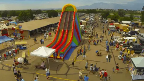 An aerial view shows a large inflatable slide set up at an outdoor market event with people walking around.