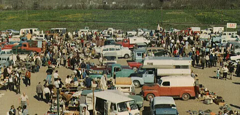 An outdoor flea market with numerous cars, vendors, and shoppers.