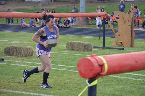 A woman running with a heavy block during an obstacle course race.