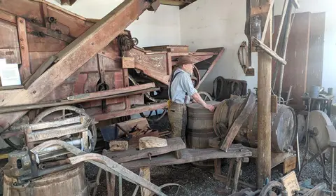 An indoor museum exhibit displaying historical farm machinery, tools, and a mannequin dressed in period attire.