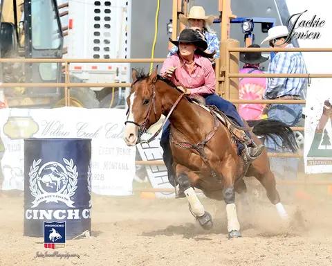 A woman rides a horse around a barrel in an arena.