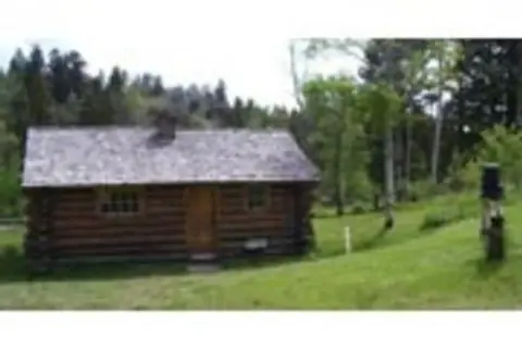 A log cabin stands in a grassy clearing surrounded by trees.