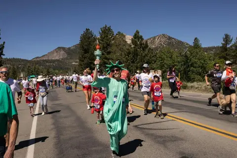 A crowd of people participating in a road race, with one runner dressed as the Statue of Liberty.