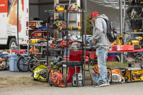 A man looks at power tools displayed on shelves and tables outdoors.