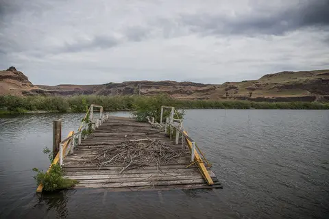 An old wooden dock sits partially submerged in a river with rolling hills in the background.