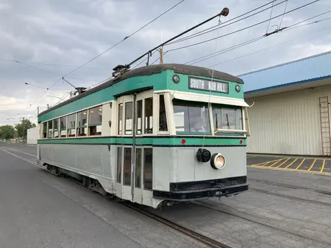 A vintage green and white trolley car sits on tracks outdoors.