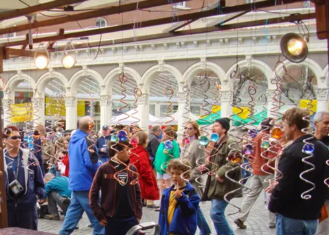 A crowd of people browses an outdoor market beneath hanging metal and glass ornaments.