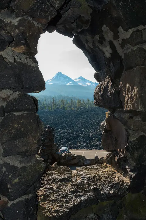 A view of snowy mountains and a lava field framed through a jagged stone opening.