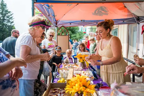 People gather at a vendor booth with pastries under an orange canopy.