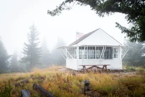 A white cabin stands in a foggy mountain landscape.