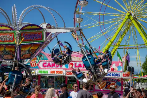 People enjoy rides and food booths at a sunny carnival.