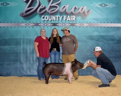 A family and a handler pose with a pig in front of a county fair backdrop.