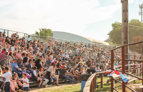 A large crowd of people seated in outdoor bleachers at an event.