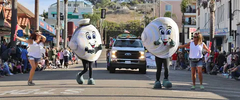 Two clam mascots walk down a street during a parade.