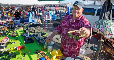 A vendor at an outdoor flea market holds up a pair of sunglasses.