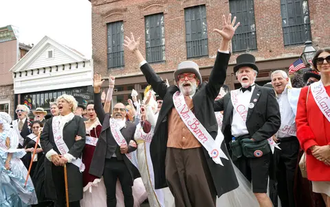 A crowd of people in historical costumes and sashes cheering outdoors.