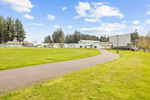 A paved path curves through grassy grounds with buildings and trees under a blue sky.